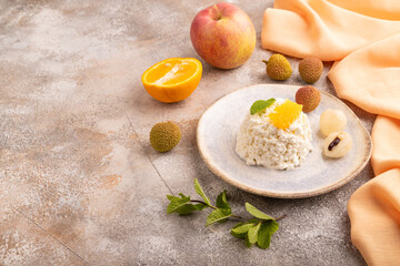 White Сottage cheese, Curd, with orange and lychee on brown concrete and orange textile, side view, copy space.