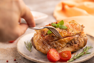 Fried Turkey Thigh with spices on plate on brown concrete with hand, orange linen textile. side view, close up, selective focus