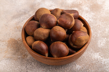 wooden bowl with raw edible Сhestnuts on brown concrete, side view, close up, minimalism