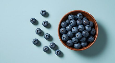 Fresh, ripe blueberries spill from a rustic wooden bowl onto a clean, pastel blue surface.