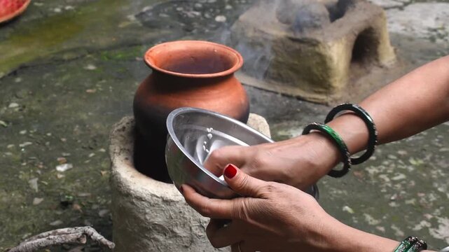 Video clip of a village woman&rsquo;s hand cooking rice in a clay pot on a traditional clay chulha stove. Represents rural lifestyle, eco-friendly cooking, Indian culture, and traditional food preparation. 