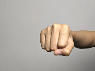 Close up of a person's fist punching forward in a clear, neutral studio setting against a grey background emphasizing the hand and its impact.