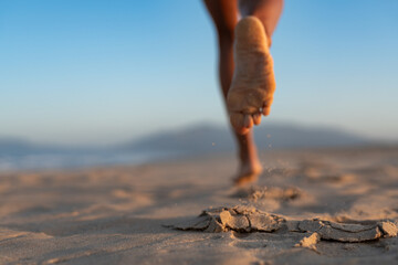 Close-up of barefoot woman's foot in motion, kicking up sand while running on beach at sunrise, dynamic fitness concept, healthy lifestyle and active outdoor morning workout.