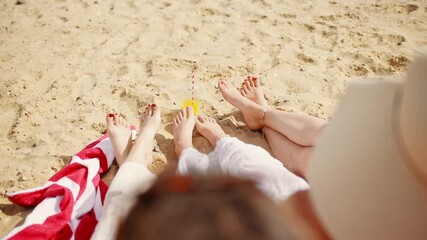 A family of three is sitting on the beach, with a woman wearing a straw hat. The woman is holding a glass of orange juice, and the other two people are sitting on a towel - Powered by Adobe