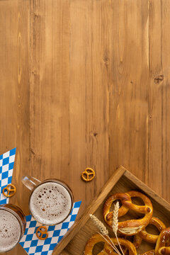 Oktoberfest-themed vertical image featuring beer mugs, salted pretzels, and festive decor on rustic wood, flatlay, top view