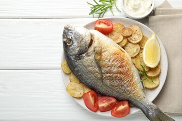 Homemade seafood dish. Tasty roasted dorado fish served with vegetables and sauce on white wooden table, flat lay. Space for text