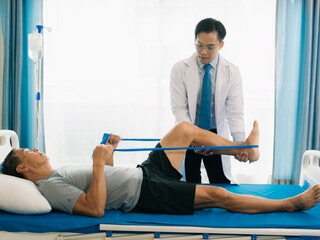 Senior Asian man using resistance band to stretch his foot muscles. Physical therapy concept of exercising with caregiver at home.