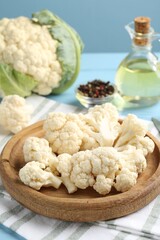 Pieces of cauliflower, peppercorns and oil on light blue wooden table, closeup