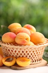 Fresh ripe apricots in wicker basket on white wooden table outdoors, closeup