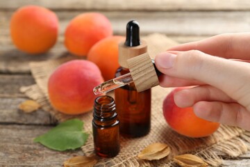 Woman dripping apricot essential oil from pipette into bottle at wooden table, closeup