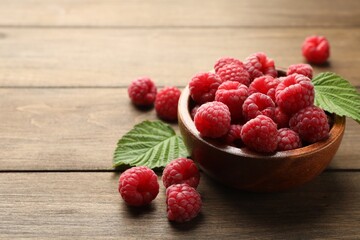 Tasty fresh ripe raspberries and leaves on wooden table, closeup. Space for text