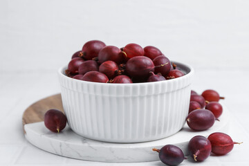 Ripe red gooseberries in bowl on white tiled table, closeup