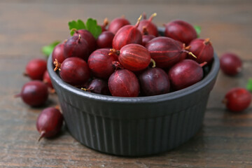 Ripe red gooseberries in bowl on wooden table, closeup