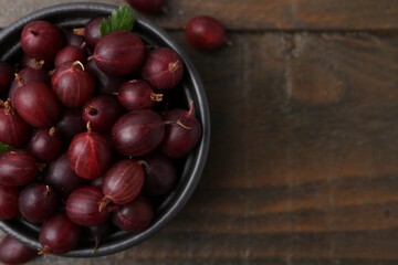 Ripe red gooseberries in bowl on wooden table, top view. Space for text