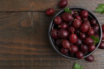 Ripe red gooseberries in bowl on wooden table, flat lay. Space for text