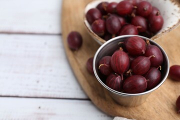 Ripe red gooseberries in bowl on white wooden table, closeup. Space for text