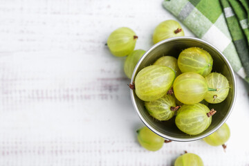 Ripe green gooseberries in bowl on white wooden table, flat lay. Space for text