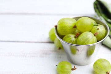 Ripe green gooseberries in bowl on white wooden table, closeup. Space for text