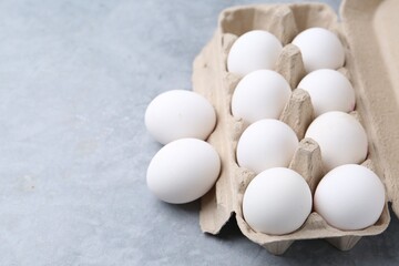 Raw chicken eggs in egg carton on grey table, closeup. Space for text