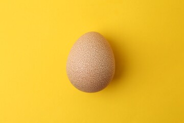 One raw chicken egg on yellow background, top view