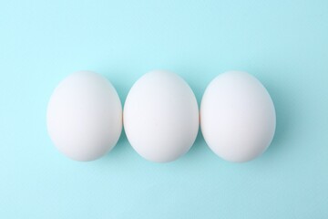Raw chicken eggs on light blue background, top view