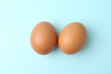 Raw chicken eggs on light blue background, top view