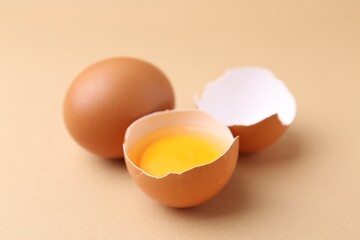 Whole and broken chicken eggs on beige background, closeup