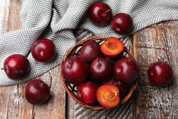 Ripe cherry plums and wicker basket on color wooden table, flat lay
