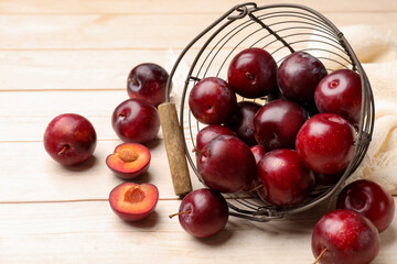 Ripe cherry plums and metal basket on light wooden table, closeup