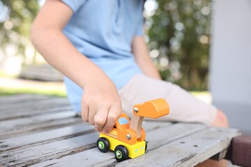 Little boy playing with toy car on wooden bench outdoors, closeup