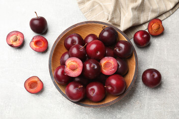 Ripe cherry plums and bowl on grey textured table, flat lay