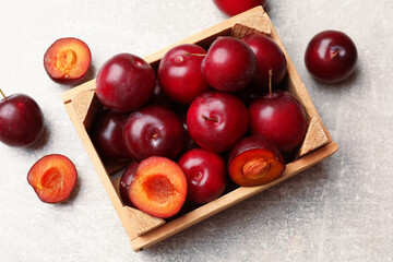 Ripe cherry plums and wooden crate on grey textured table, flat lay