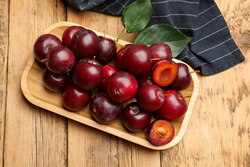 Ripe cherry plums, green leaves and cloth on wooden table, flat lay