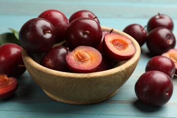 Whole, cut cherry plums and bowl on light blue wooden table, closeup