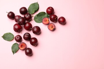 Whole, cut cherry plums and green leaves on pink background, flat lay. Space for text