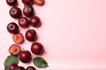 Whole, cut cherry plums and green leaves on pink background, flat lay. Space for text
