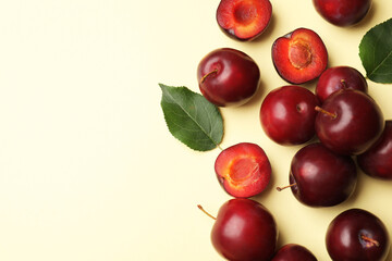 Whole, cut cherry plums and green leaves on light yellow background, flat lay. Space for text