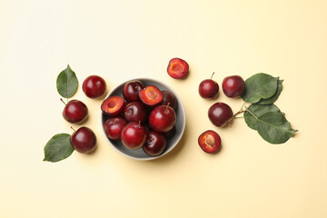 Whole, cut cherry plums, bowl and green leaves on light yellow background, flat lay