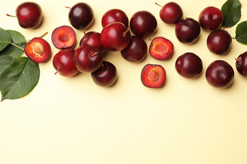 Whole, cut cherry plums and green leaves on light yellow background, flat lay. Space for text