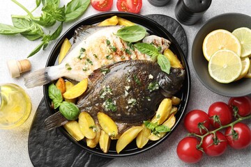 Tasty roasted flounder fish with herbs, potato, lemon slices and tomatoes on light table, flat lay. Homemade seafood dish