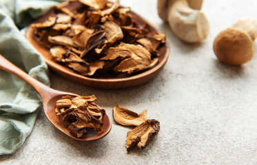 Dried mushrooms on wooden spoon and bowl, fresh mushrooms on grey table