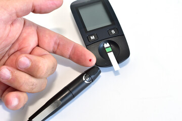A man is about to apply a drop of his blood to a test strip inserted into a glucometer.