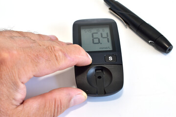 A man's hand turns on a glucometer, and a device for puncturing the skin lies nearby.