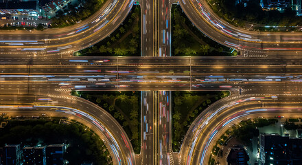 Aerial view showcases a highway interchange at night, with vibrant light trails from moving vehicles.