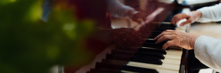 Obraz premium Elderly Hands Playing Piano Keys Wide Banner