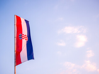 Croatian national flag waving on pole with clear evening sky and light clouds in background.
