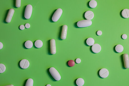 A variety of medications, including white round and oval tablets and a single red one, are scattered randomly on a bright lime-green background. This pattern symbolizes modern medicine and health, hig