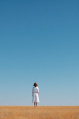 Obraz premium figure in white dress stands in golden field under vast blue sky