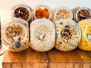 lass jars filled with cereals, granola, oats, dried fruits and nuts on a wooden buffet table. Nutrition, choice, wellness and variety in hotel breakfast dining service.
