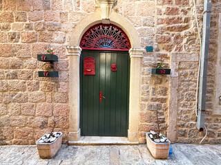 A green wooden door with red mailbox and arched stone frame on a rustic wall. Architecture, tradition, entrance and residential identity in urban street facade.